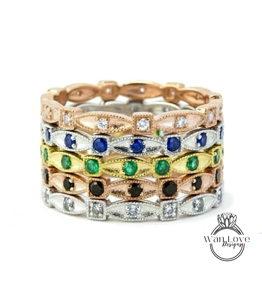 A stack of rings with various colored gemstones, including diamonds and emeralds, set in a metallic band.