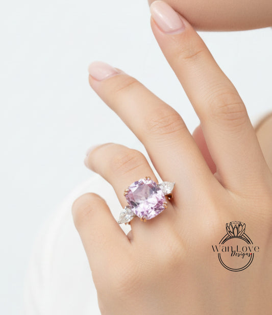 A close-up of a person's hand wearing a large, pink gemstone ring with a logo in the bottom right corner.