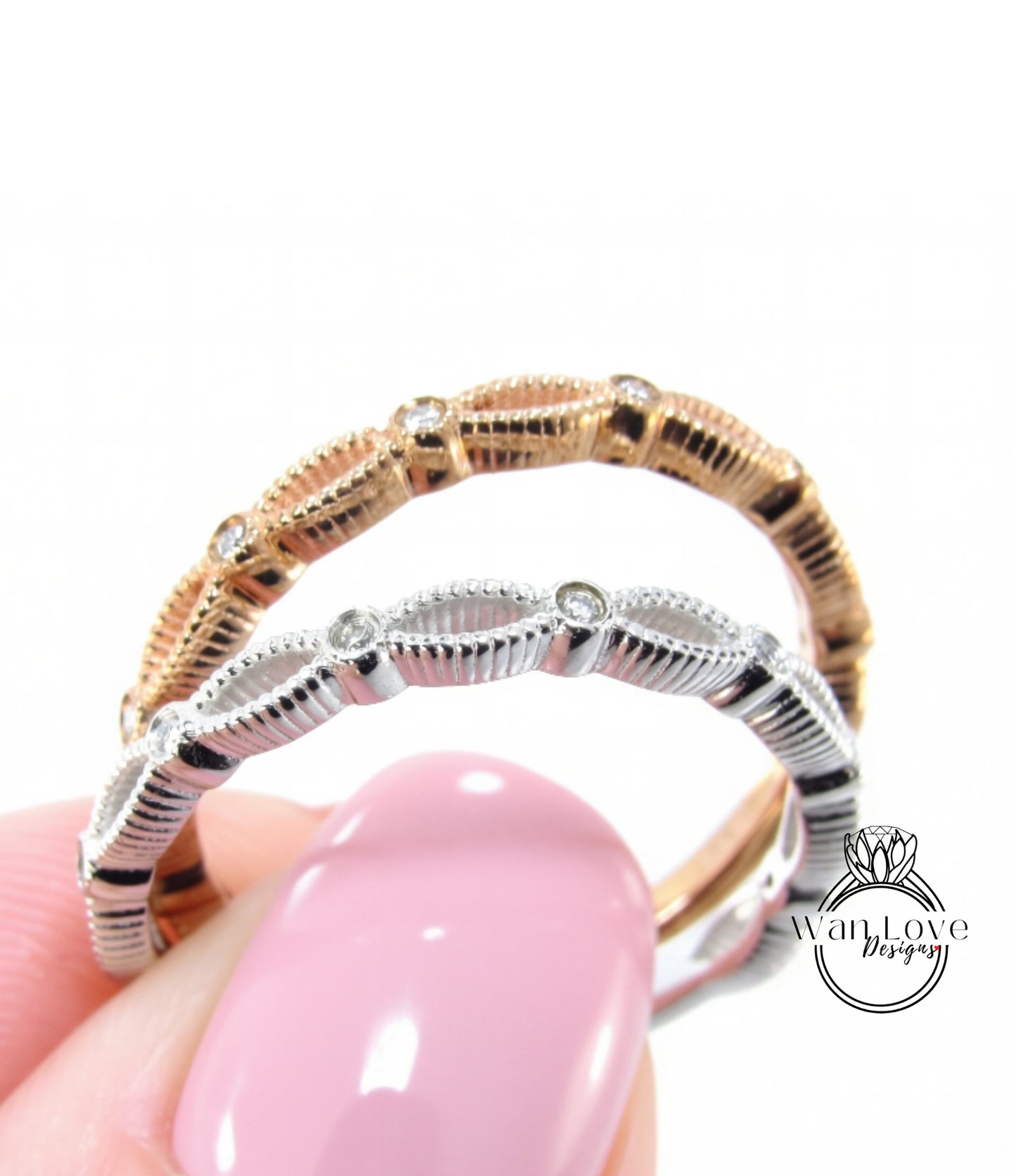 A close-up of a person's hand holding a ring with a pink background and two rings, one gold and one silver, with a pink nail polish.