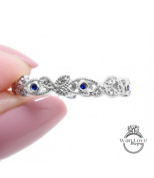 A hand holding a silver ring with blue gemstones, against a white background.
