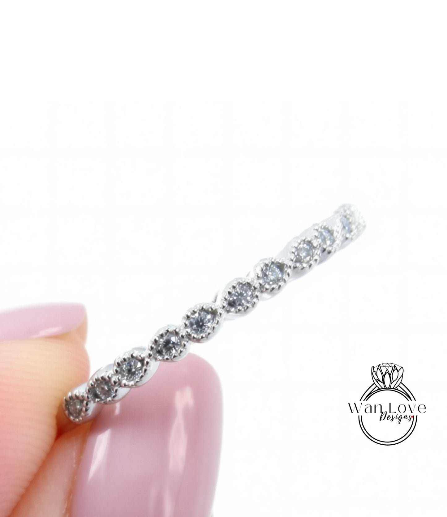 A close-up view of a person's hand holding a silver ring with a row of small diamonds on it.
