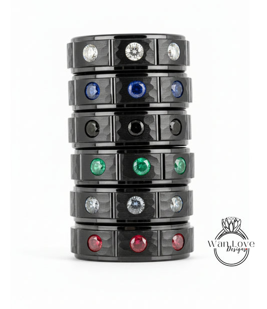 A stack of black rings with various colored gemstones, including diamonds, set in the center of each ring.