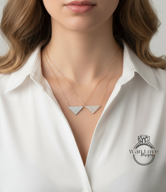 A close-up of a woman wearing a white collared shirt with a delicate necklace featuring two triangular pendants.