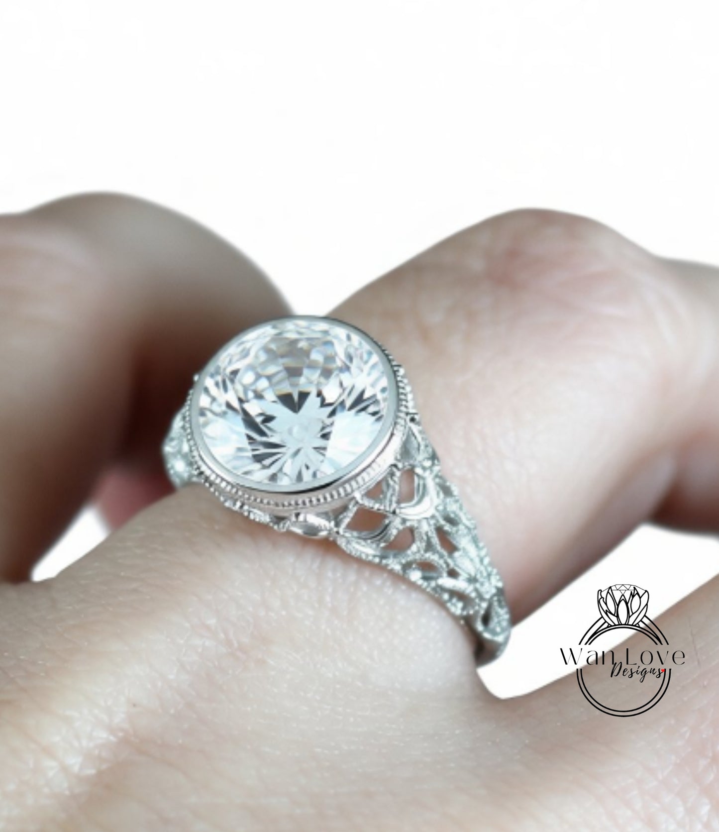 A close-up of a person's hand wearing a diamond engagement ring with a large central diamond surrounded by smaller diamonds and a decorative metal band.