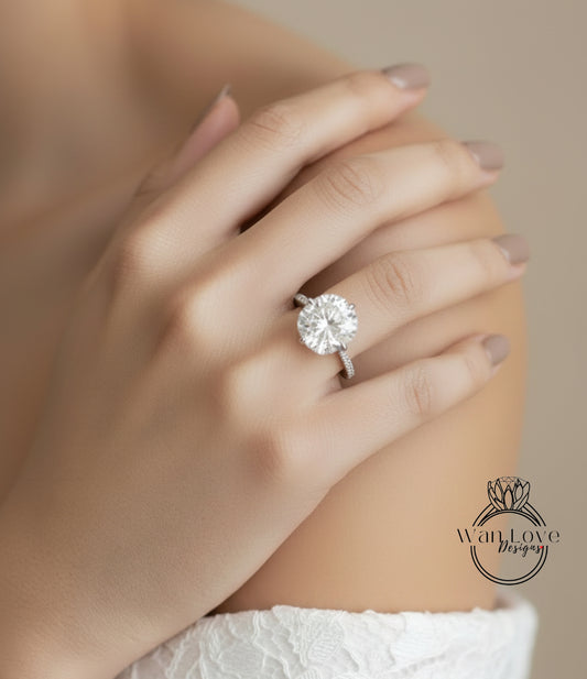 A close-up of a person's hand wearing a large, round diamond engagement ring on the ring finger.