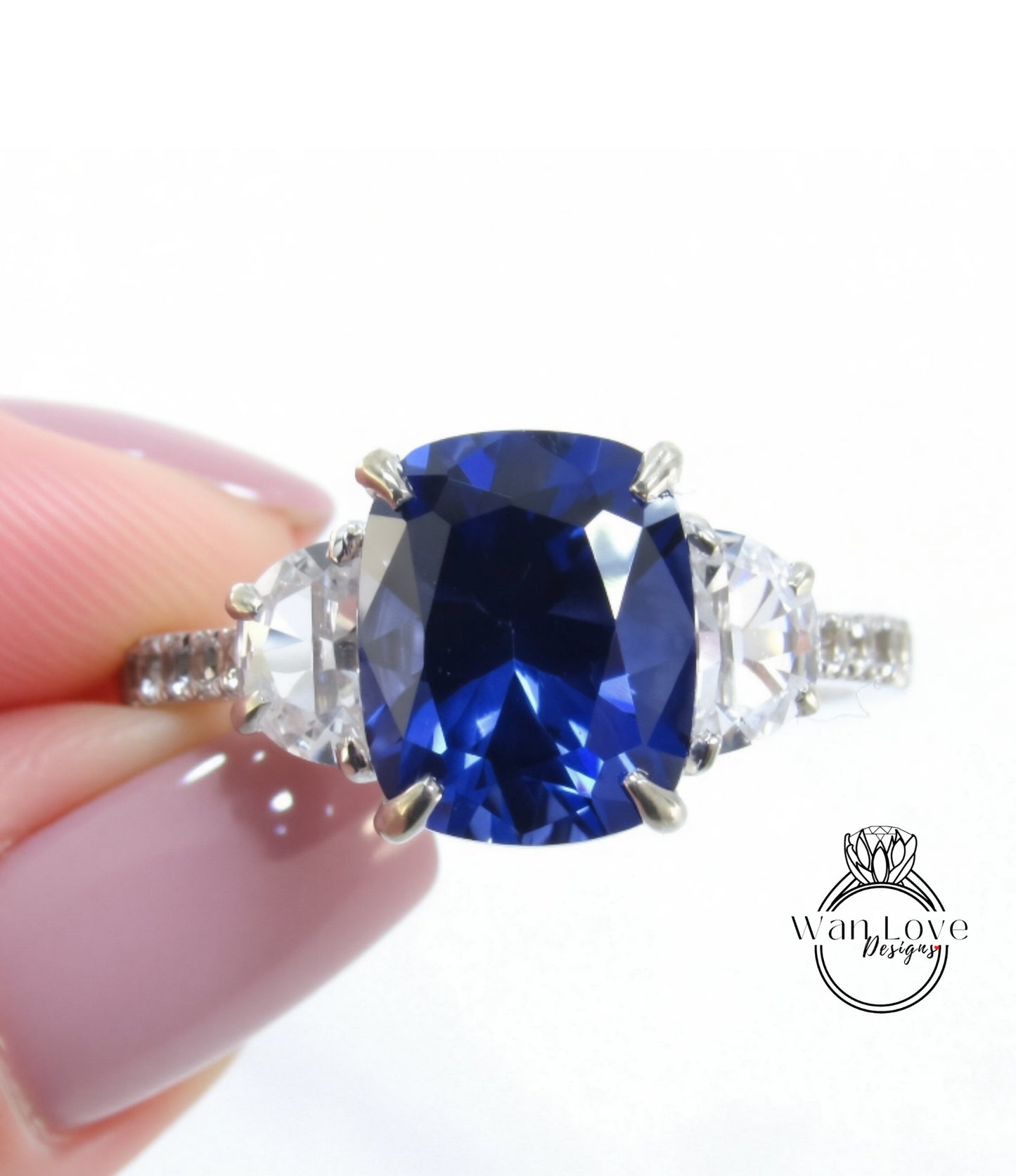 A close-up of a person's hand holding a diamond ring with a large blue gemstone.