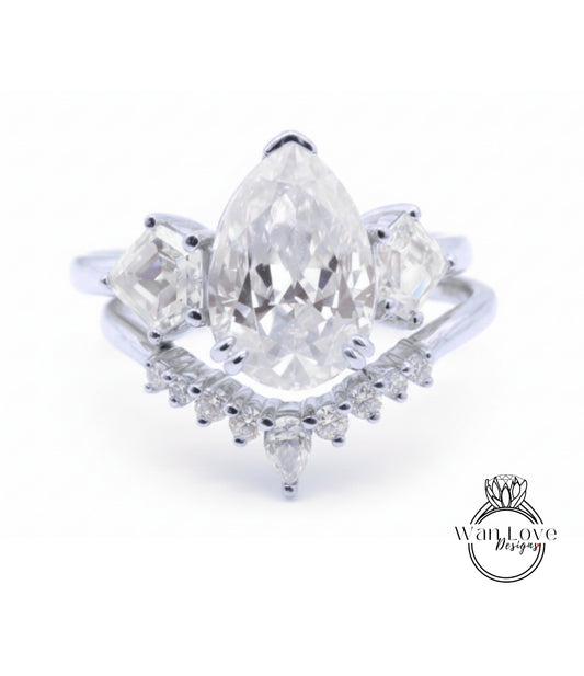 A close-up image of a diamond engagement ring with a large pear-shaped diamond at the center, surrounded by smaller diamonds on either side.