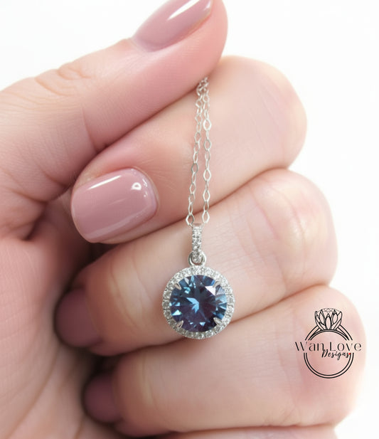 A hand holding a silver necklace with a blue gemstone pendant.