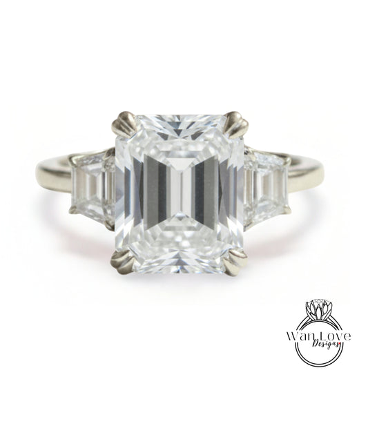 A large, clear diamond engagement ring with a prominent central diamond surrounded by smaller diamonds on either side.