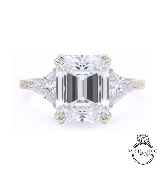 A large, clear diamond engagement ring with a prominent central diamond surrounded by smaller diamonds on either side.