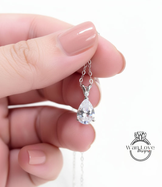 A hand holding a delicate necklace with a single, large, clear gemstone pendant.