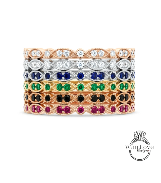 A stack of rings with various colored gemstones, including diamonds and gemstones, set in a rose gold or silver metal band.
