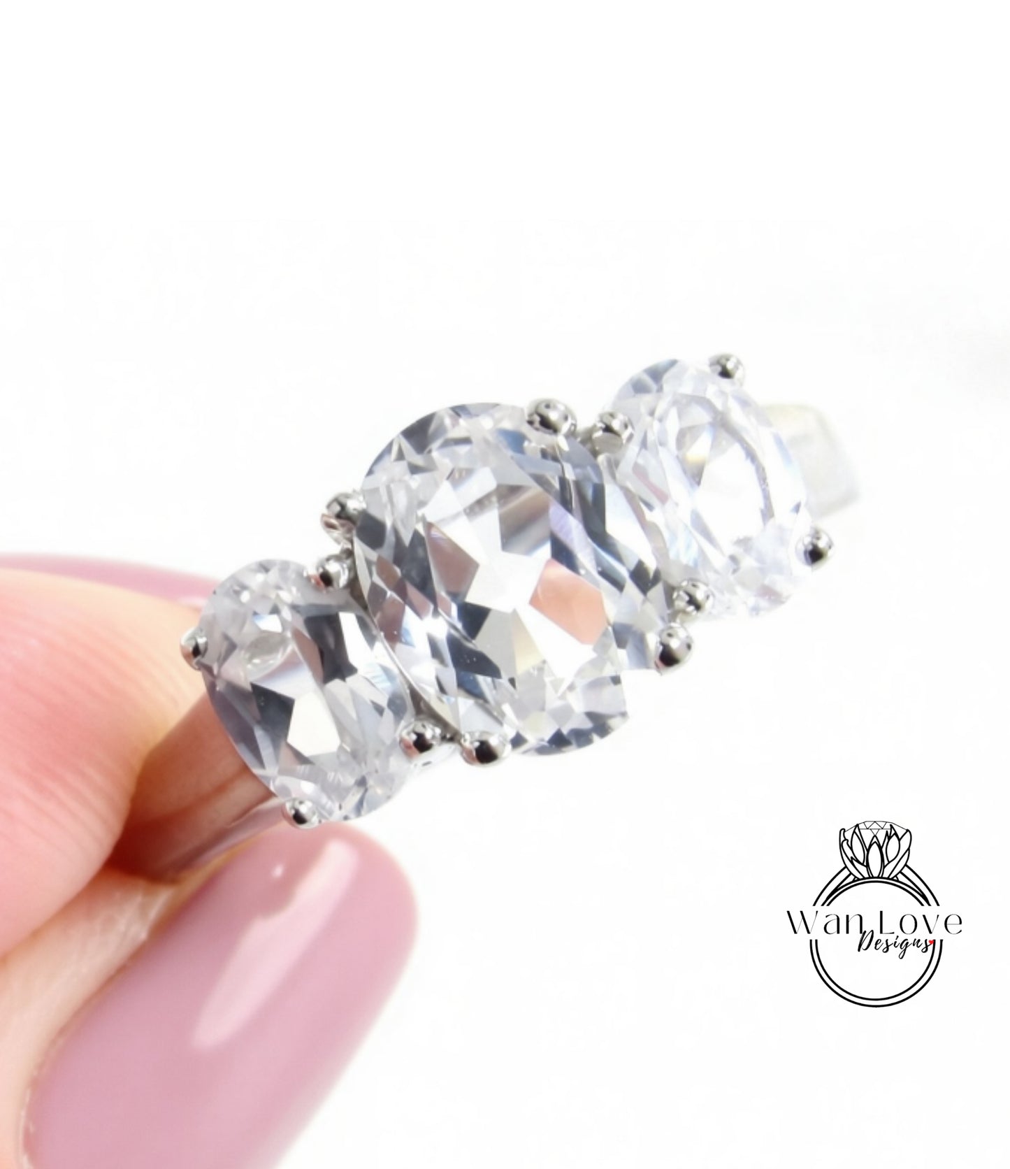 A close-up of a person's hand holding a ring with three large, clear gemstones.