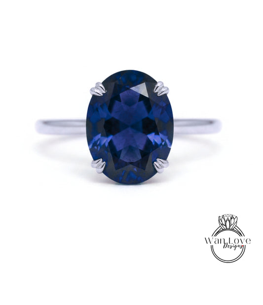 A close-up image of a silver ring with a large, deep blue gemstone, likely a sapphire, set in the center of the band.