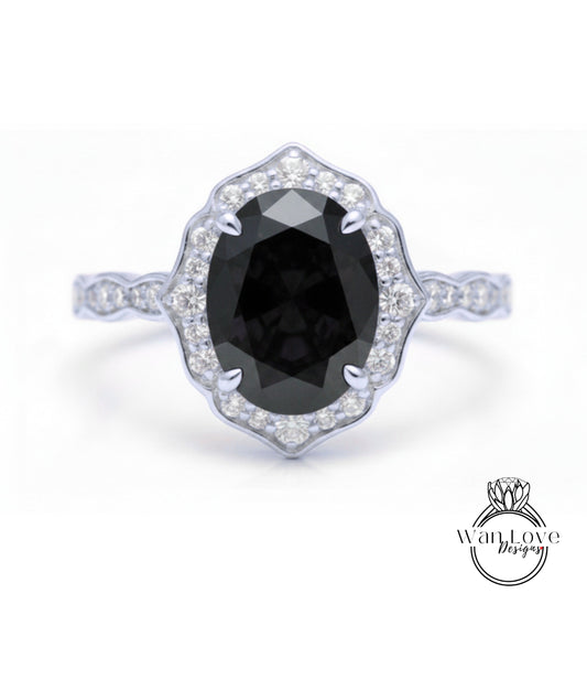 A silver ring with a large oval-shaped black gemstone at the center, surrounded by smaller diamonds.