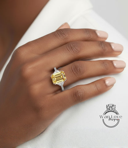 A close-up of a person's hand wearing a large yellow diamond ring on the ring finger.