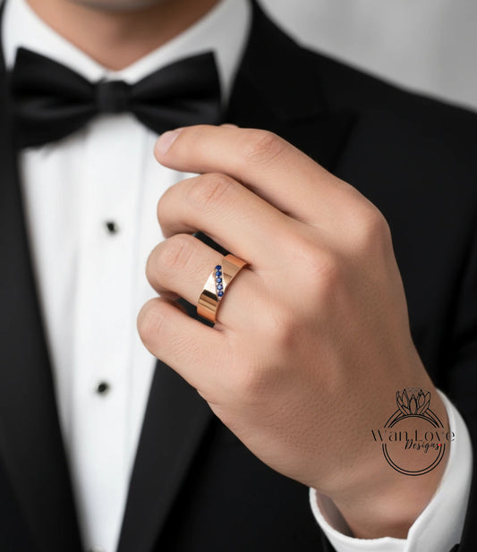 A close-up of a man's hand wearing a gold ring with blue gemstones, wearing a black tuxedo with a bow tie.