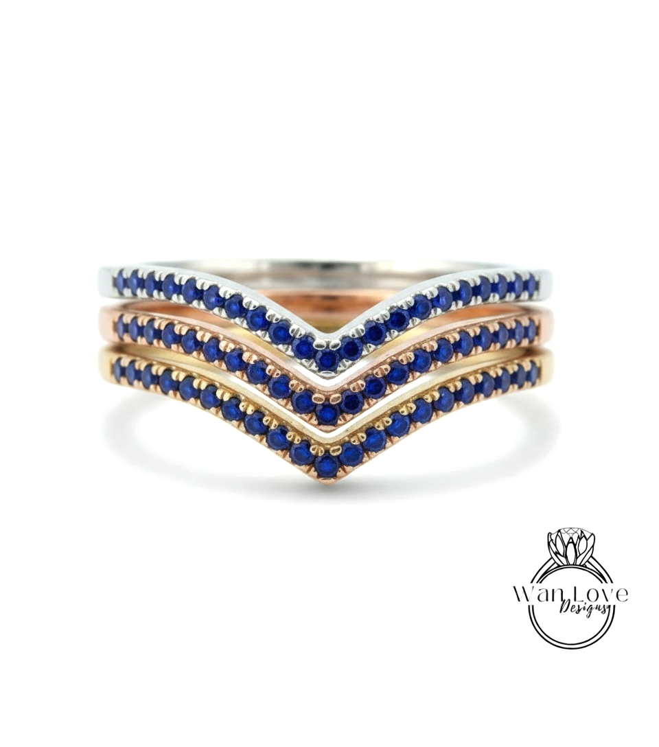 A ring with three layers of rings, each with blue gemstones. The topmost ring is silver, the middle ring is gold, and the bottom ring is rose gold. The gemstones are blue, and the rings are arranged in a v-shape.
