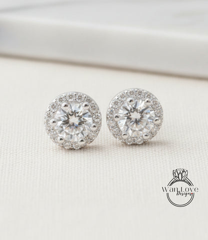 A pair of elegant diamond earrings with a large central diamond surrounded by smaller diamonds, resting on a white surface.