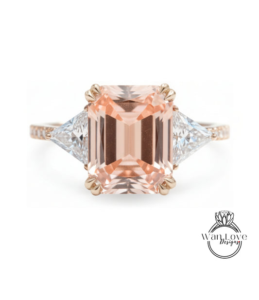 A large, peach-colored gemstone engagement ring with a gold band and two smaller diamonds on either side.