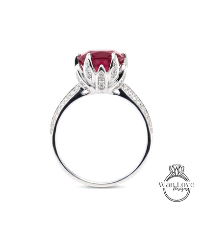 A silver ring with a large, red gemstone, likely a diamond, set in a flower-like design.