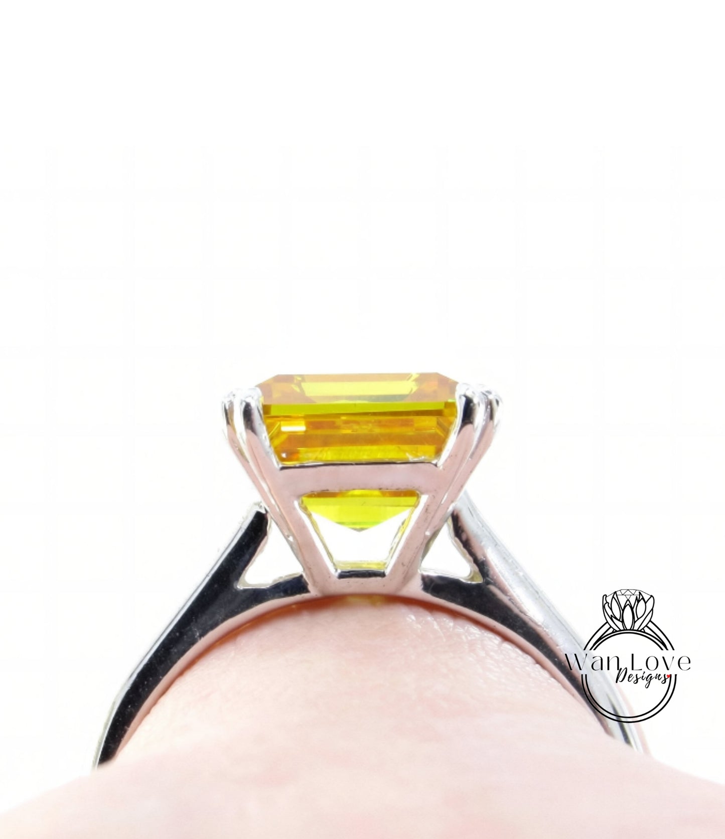 A close-up view of a silver ring with a large yellow gemstone, likely an emerald, set in the center of the band.