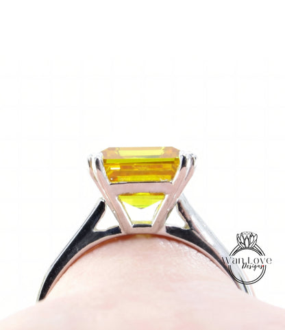 A close-up view of a silver ring with a large yellow gemstone, likely an emerald, set in the center of the band.