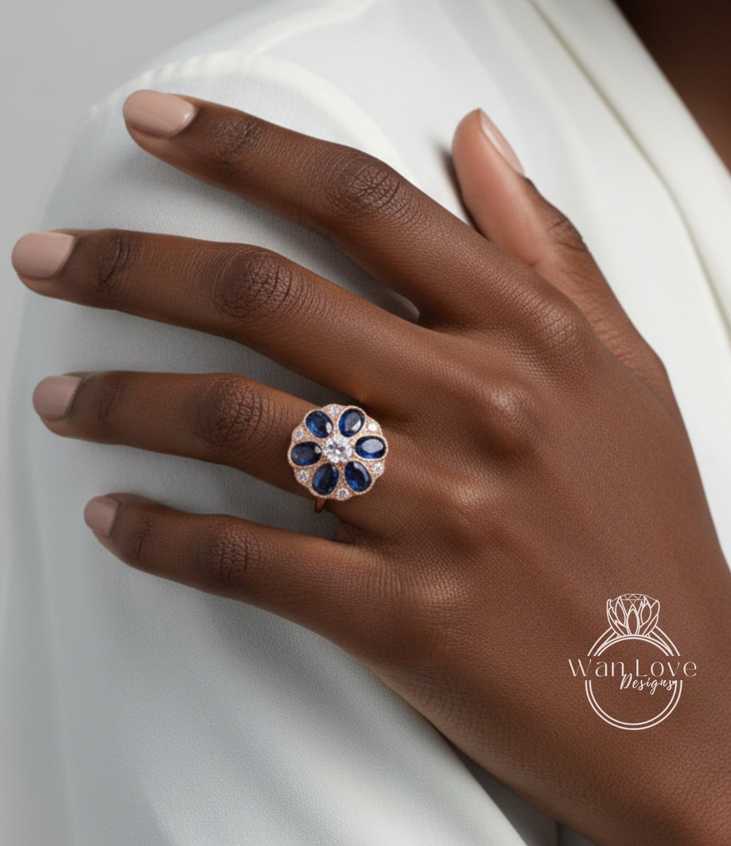 A close-up of a person's hand wearing a ring with a blue flower design and a large gemstone.