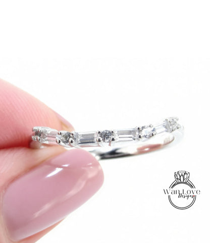 A close-up of a person's hand holding a silver ring with a row of small diamonds on it.