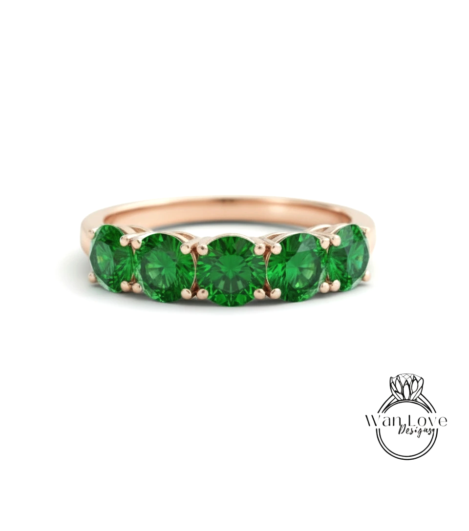 A gold ring with a row of green gemstones, likely emeralds, set in the band.