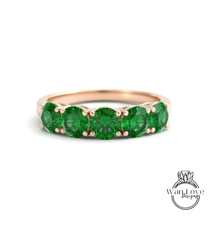 A gold ring with a row of green gemstones, likely emeralds, set in the band.