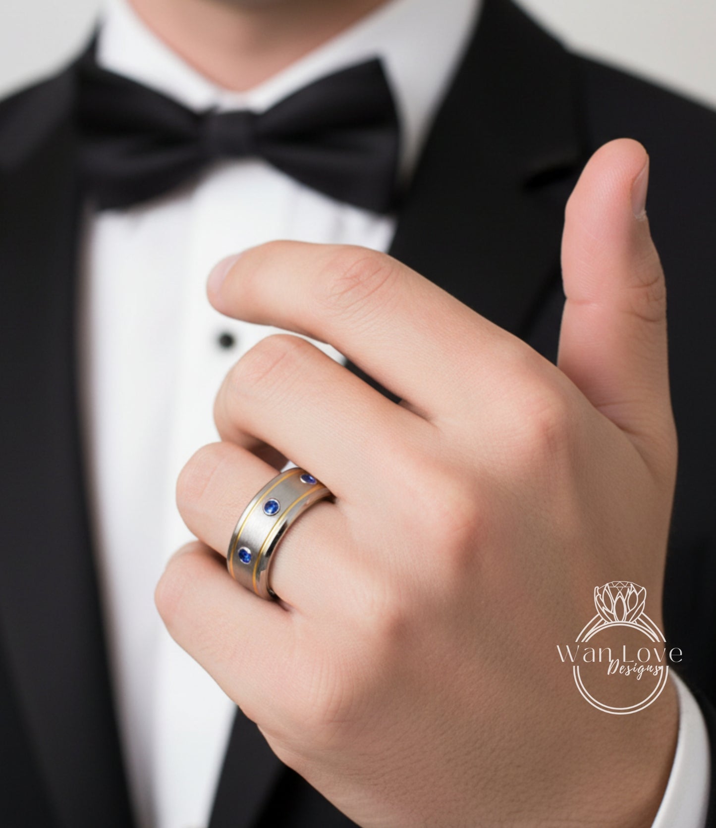 A close-up of a person's hand wearing a gold and blue ring, with a black bow tie visible.