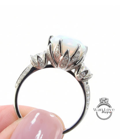 A close-up of a person's hand holding a silver ring with a large opal gemstone and intricate floral designs.