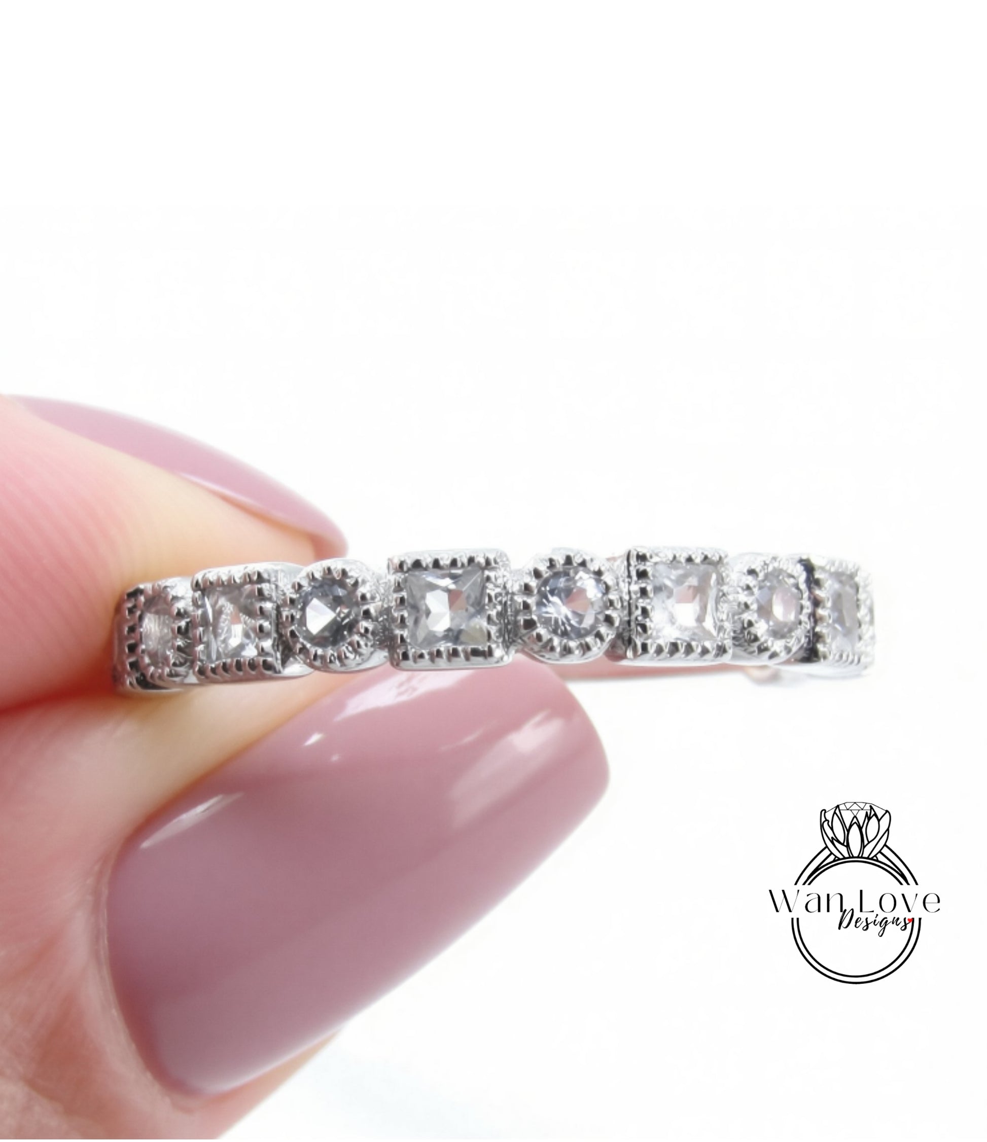 A close-up image of a person's hand holding a silver ring with a row of small diamonds on it.