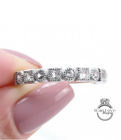 A close-up image of a person's hand holding a silver ring with a row of small diamonds on it.
