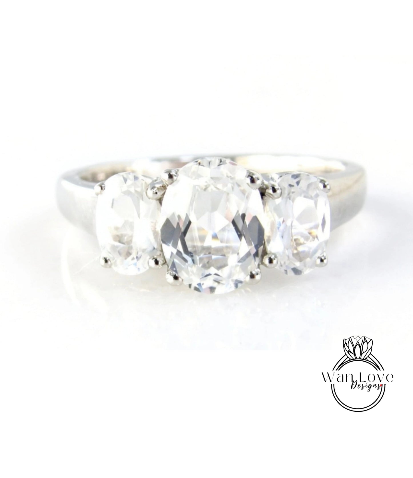 A close-up image of a silver ring with three large, clear gemstones set in the band.