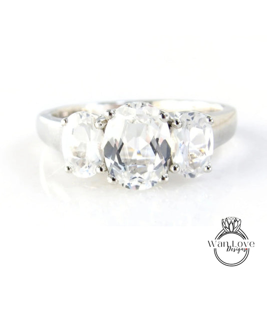 A close-up image of a silver ring with three large, clear gemstones set in the band.