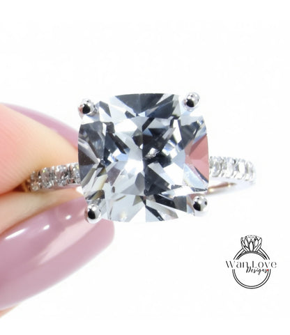 A close-up of a person's hand holding a diamond engagement ring with a large, clear gemstone.