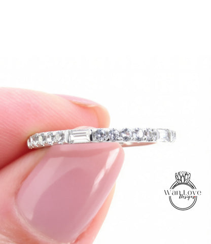 A close-up image of a person's hand holding a ring with a row of small diamonds along the band.