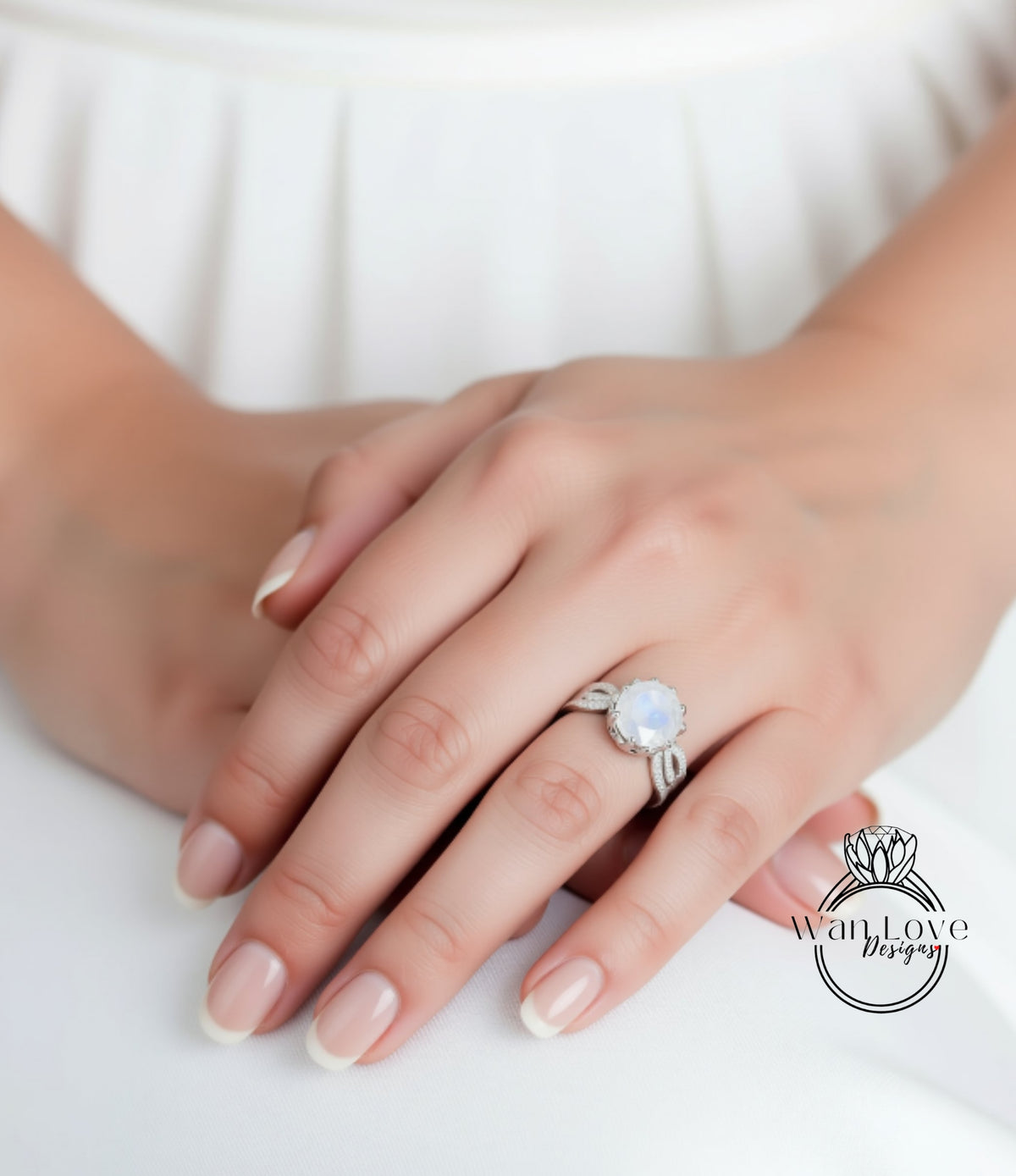 A close-up of a person's hands wearing a ring with a large moonstone.