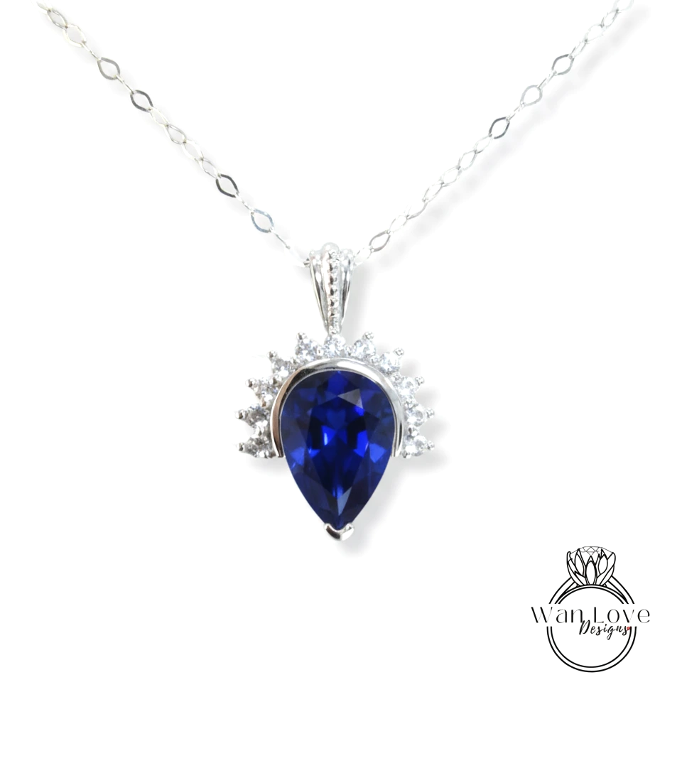 A silver necklace with a large blue gemstone pendant, which appears to be a sapphire.