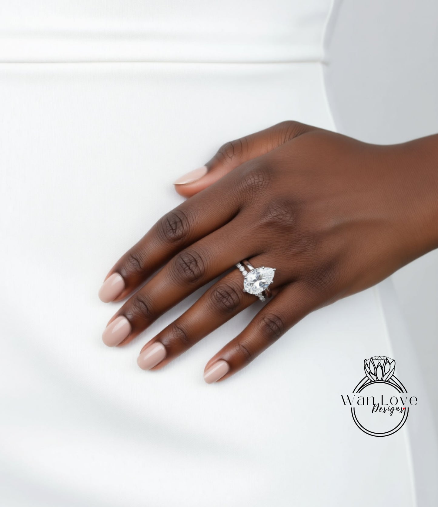 A close-up of a hand wearing a diamond engagement ring, with a white dress visible in the background.