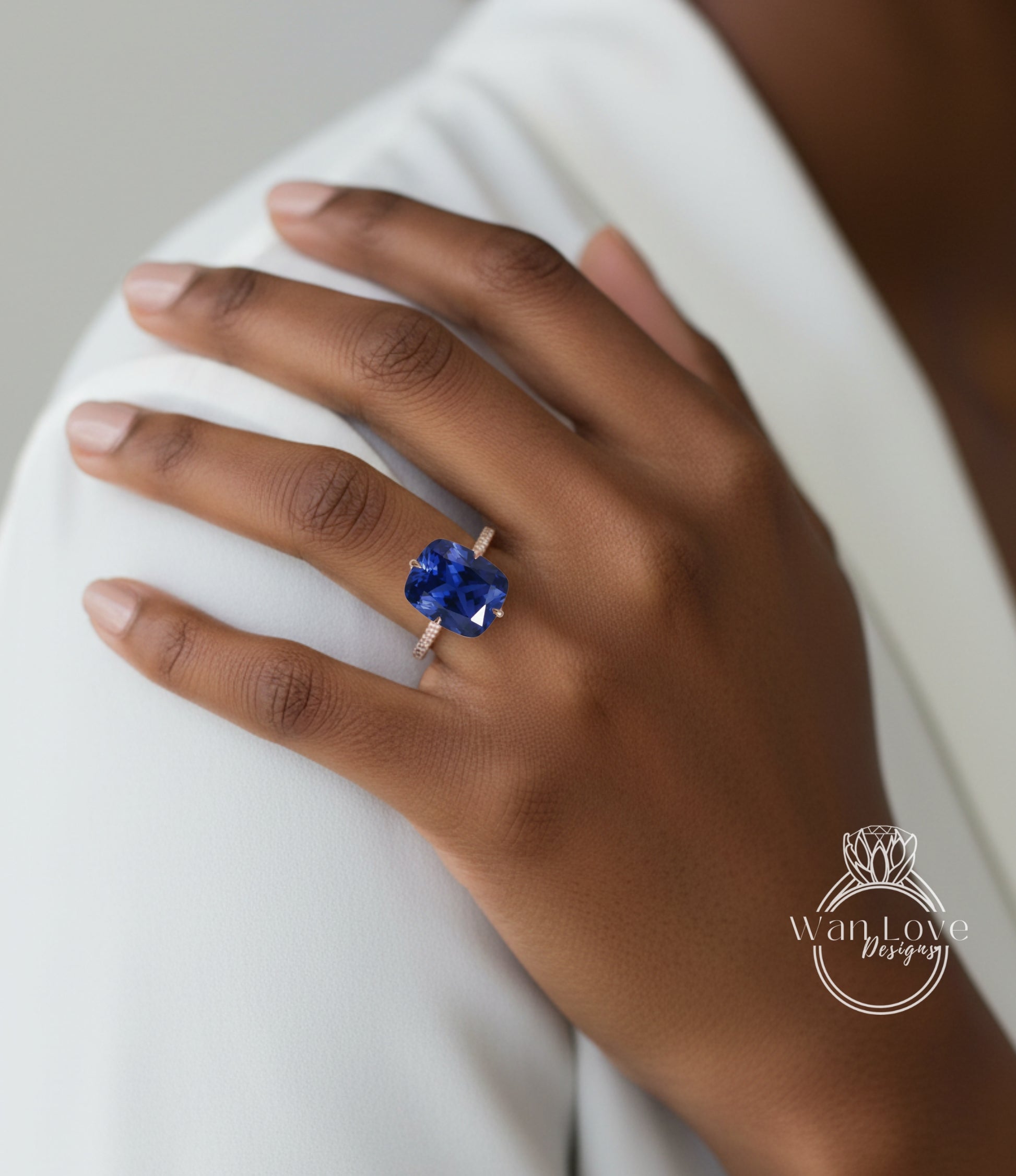 A close-up of a hand wearing a ring with a large blue gemstone, resting on a white sleeve.