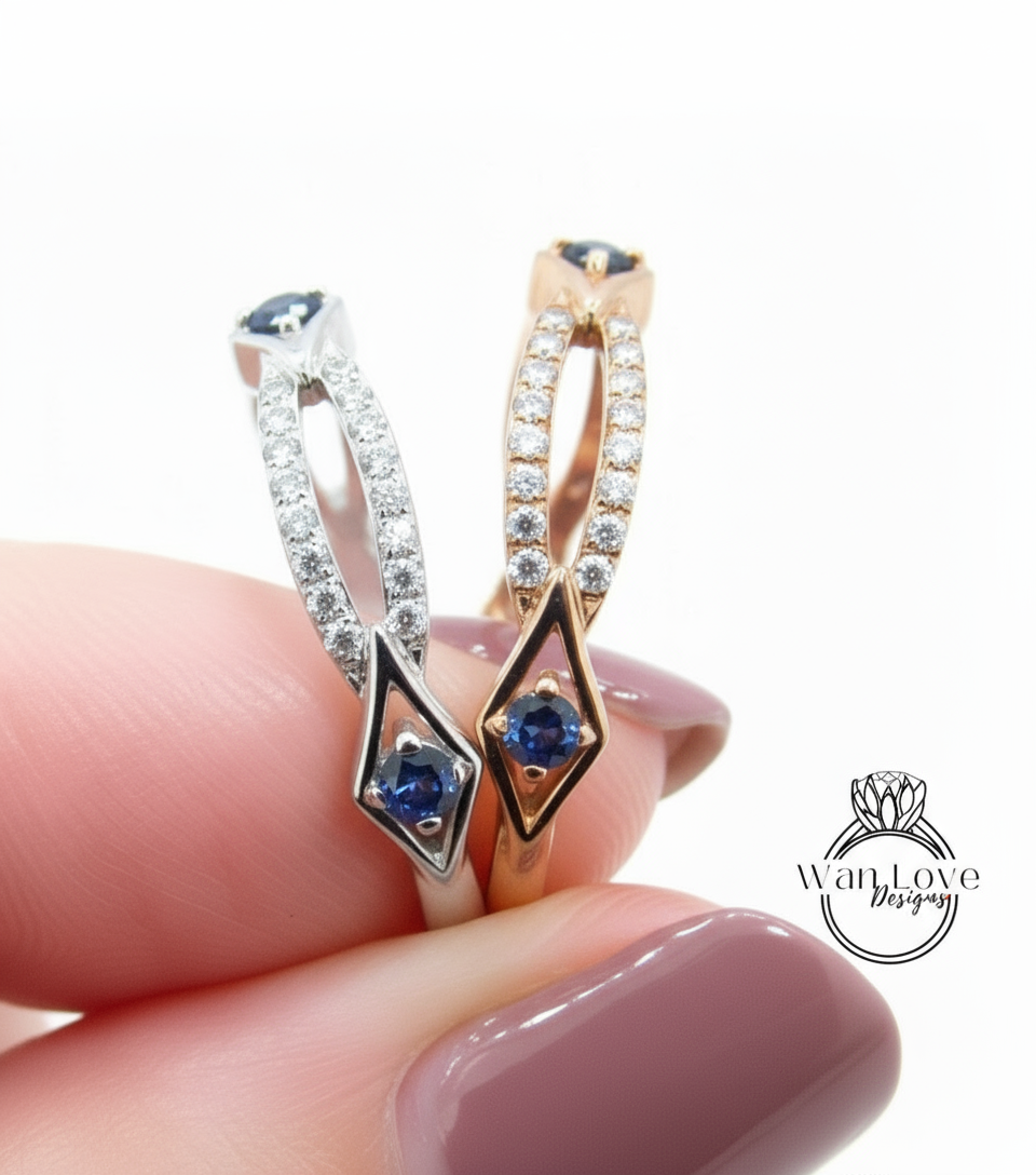 A close-up of a person's hand holding a ring with two diamond-encrusted designs featuring blue gemstones.