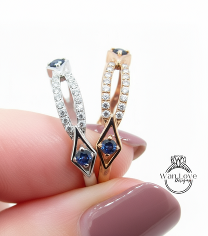A close-up of a person's hand holding a ring with two diamond-encrusted designs featuring blue gemstones.