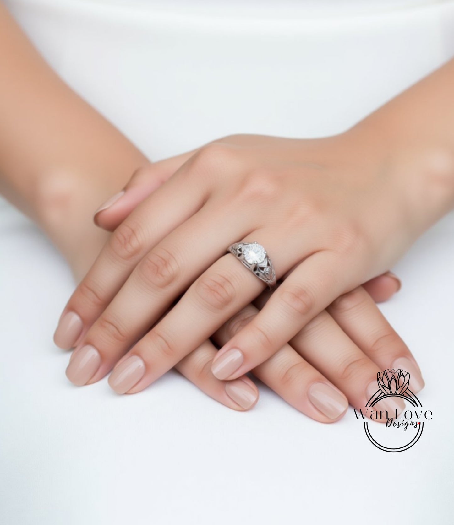A close-up image of a person's hands with a ring on the finger, resting on a white surface.