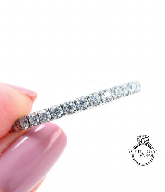 A hand holding a diamond band ring with a row of clear gemstones.
