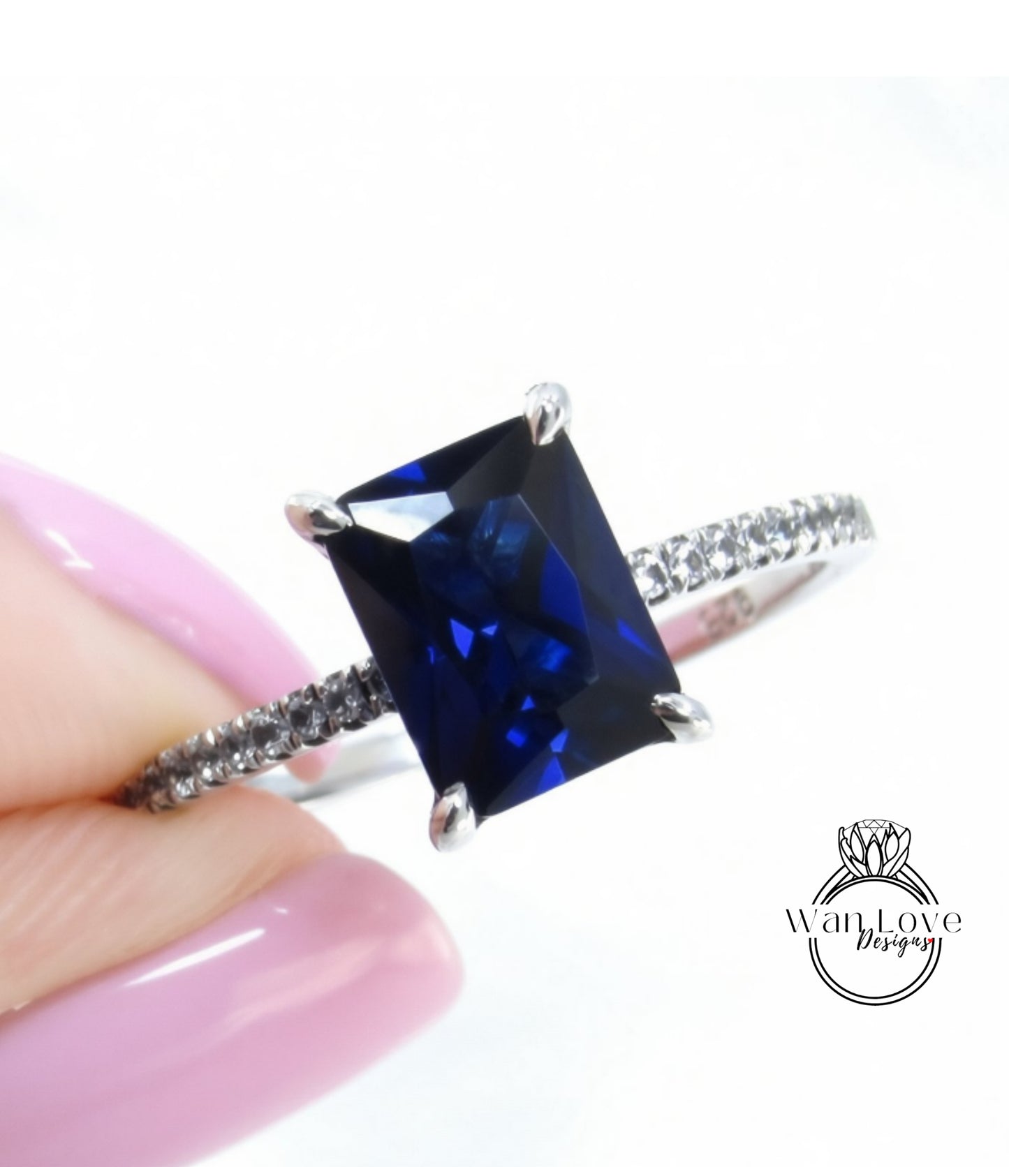 A close-up image of a person's hand holding a ring with a large blue gemstone, likely a sapphire, set in a silver band.
