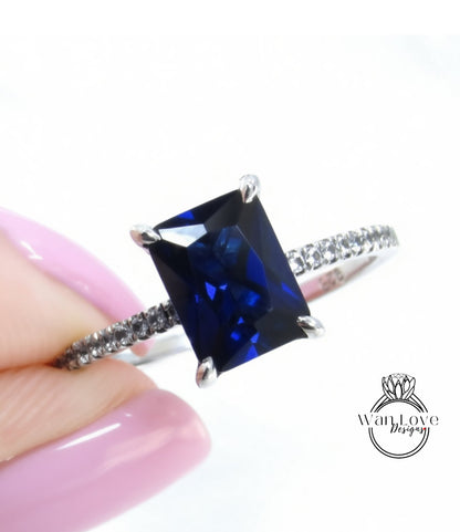 A close-up image of a person's hand holding a ring with a large blue gemstone, likely a sapphire, set in a silver band.