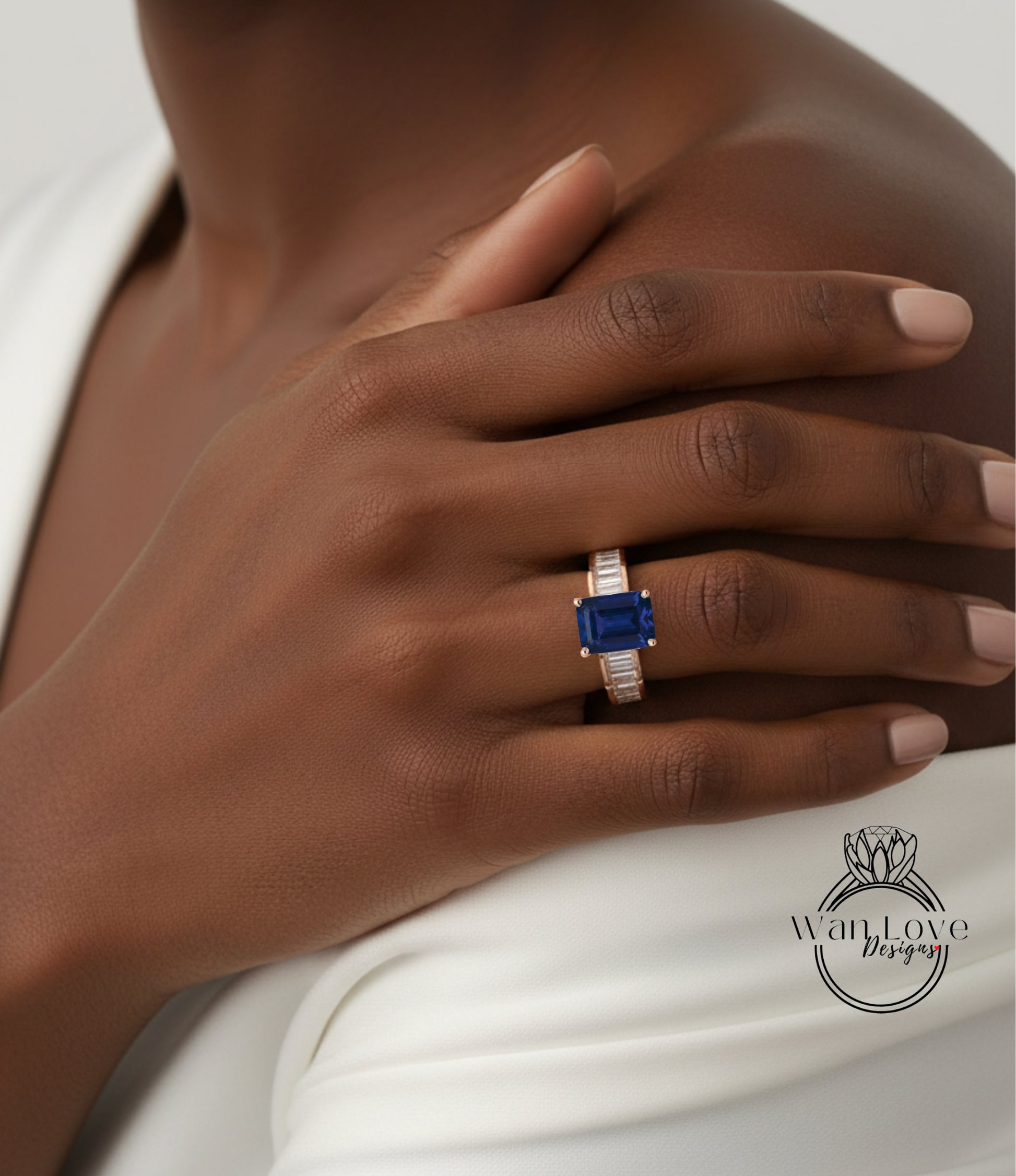 A close-up of a person's hand wearing a ring with a blue gemstone, resting on a white surface.